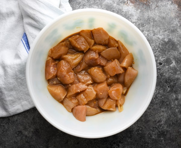 Marinating chunks of chicken in a white bowl