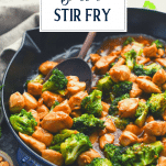 Side shot of a pan of chicken broccoli stir fry with text title overlay