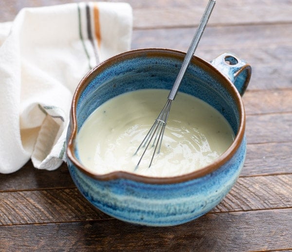 Creamy salad dressing in a blue mixing bowl with whisk