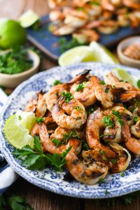 Close up side shot of the best grilled shrimp recipe garnished with parsley and limes on a blue and white plate