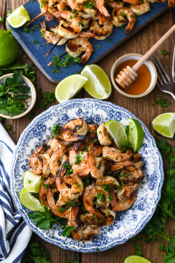 Overhead image of grilled shrimp on a blue and white plate with lime wedges