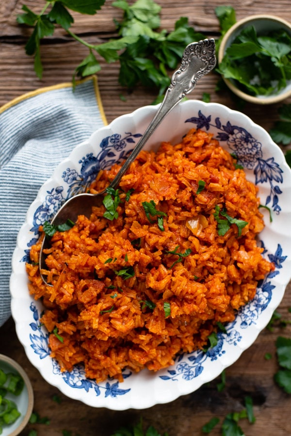 Easy red rice recipe on a wooden table with parsley garnish nearby