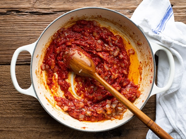 Stirring tomato paste bacon and onion in a skillet