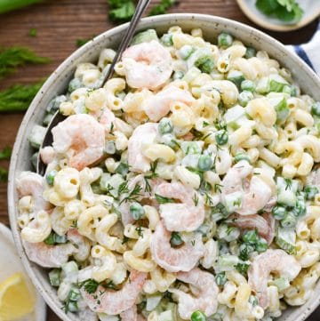 Close overhead image of a bowl of lemon shrimp pasta salad surrounded by fresh parsley and lemons on the table