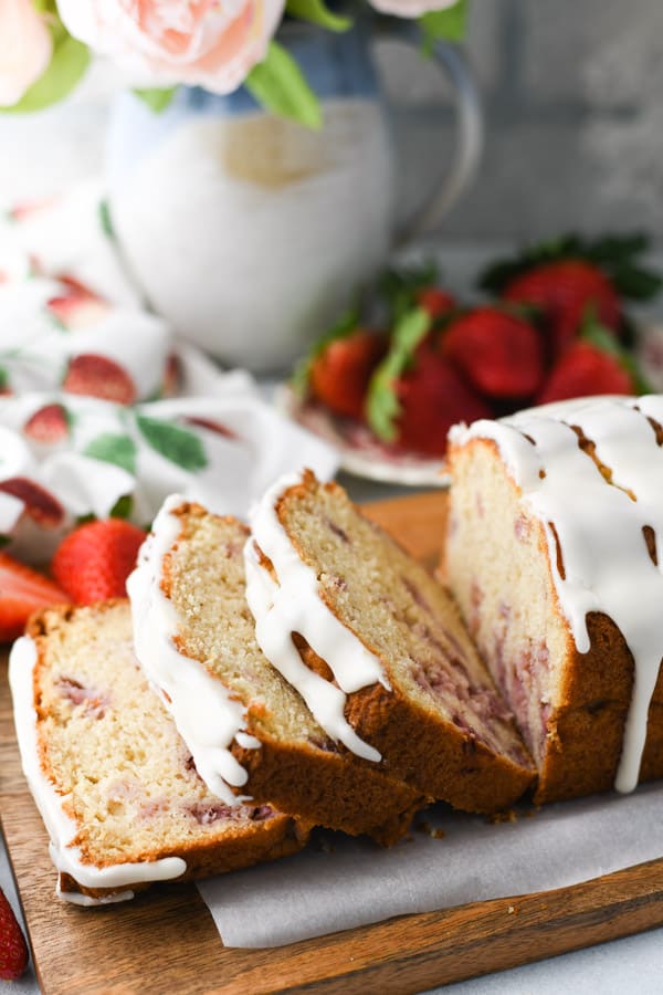 Side shot of a loaf of strawberry bread on a white tray with fresh berries in the background