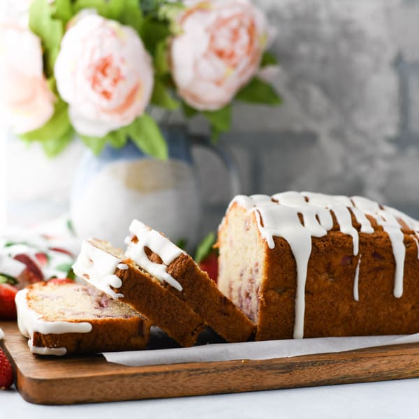 Square image of glazed strawberry bread in front of a white brick wall