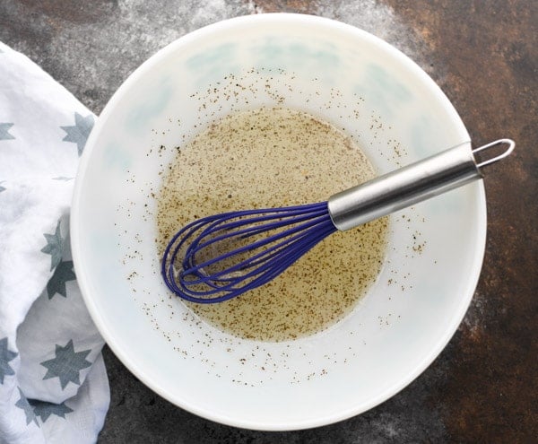 Vinegar based dressing for coleslaw in a white bowl with a blue whisk