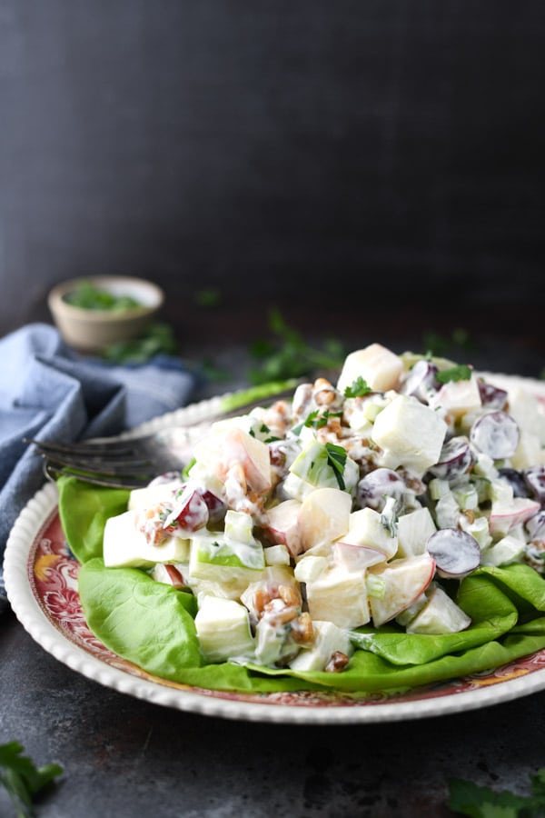 An easy Waldorf Salad recipe served on a bed of lettuce in front of a dark backdrop.