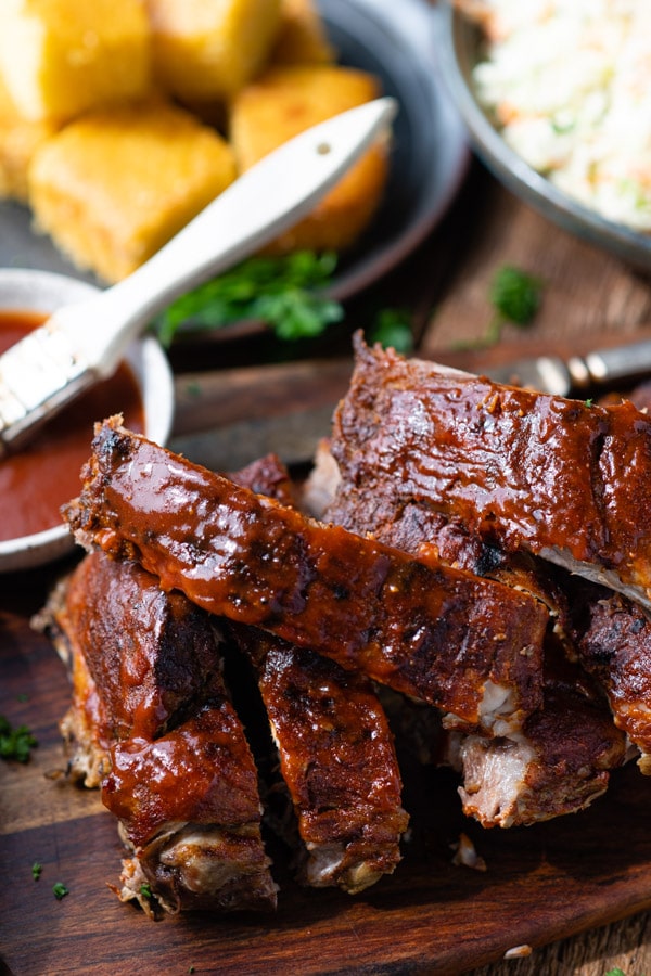 Tender pieces of BBQ baby back ribs covered in a tangy BBQ sauce served on a wooden cutting board.