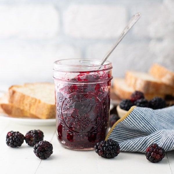 Square side shot of a jar of blackberry jam with pectin on a white table