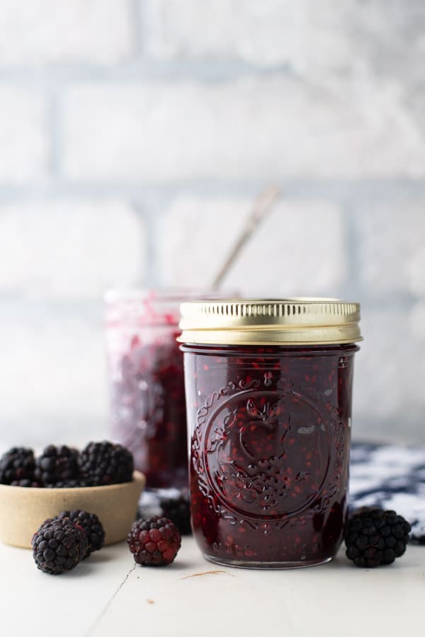 Side shot of two jars of small batch blackberry jam on a white table