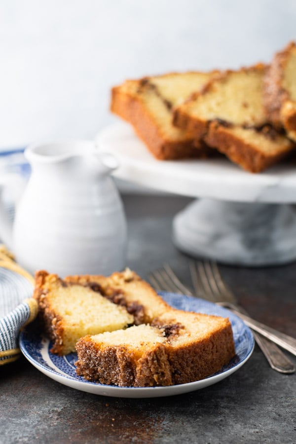 Slice of cinnamon swirl bread on a blue and white plate with cake stand in the background