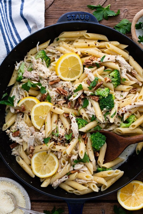 Overhead image of a wooden spoon in a cast iron skillet full of easy creamy pesto chicken pasta