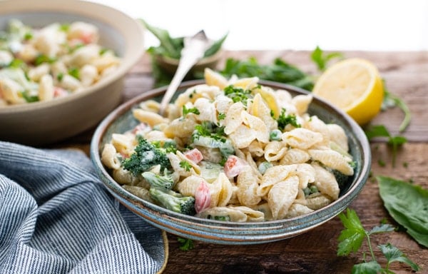 Horizontal image of creamy pasta salad with mayo on a blue stoneware bowl with fresh herbs garnished on top