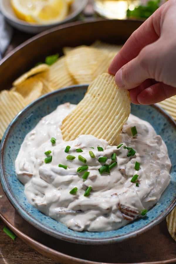Hand dipping a potato chip in a bowl of sour cream and onion dip