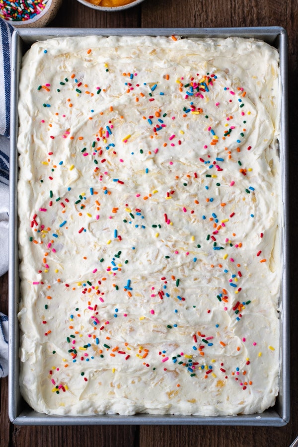 An overhead image of a completed Pig Pickin' Cake, topped with fluffy pineapple frosting and multicolored sprinkles.