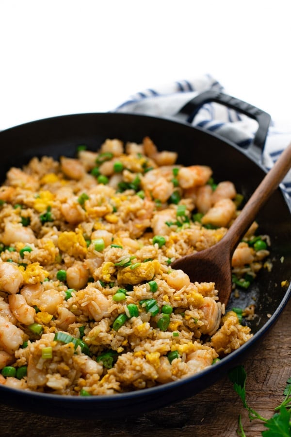Close up side shot of a skillet of Chinese shrimp fried rice with a wooden spoon