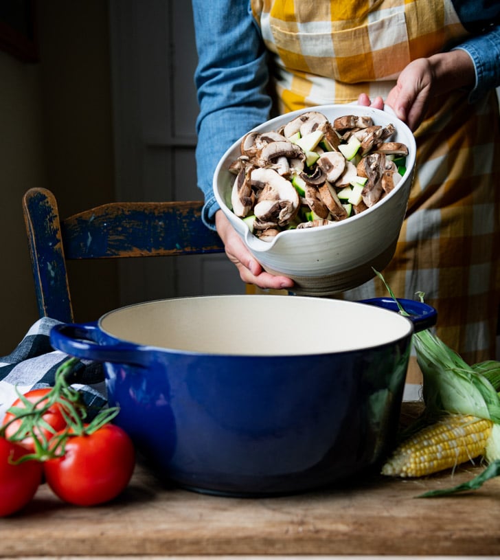 Adding fresh vegetables to a blue Dutch oven