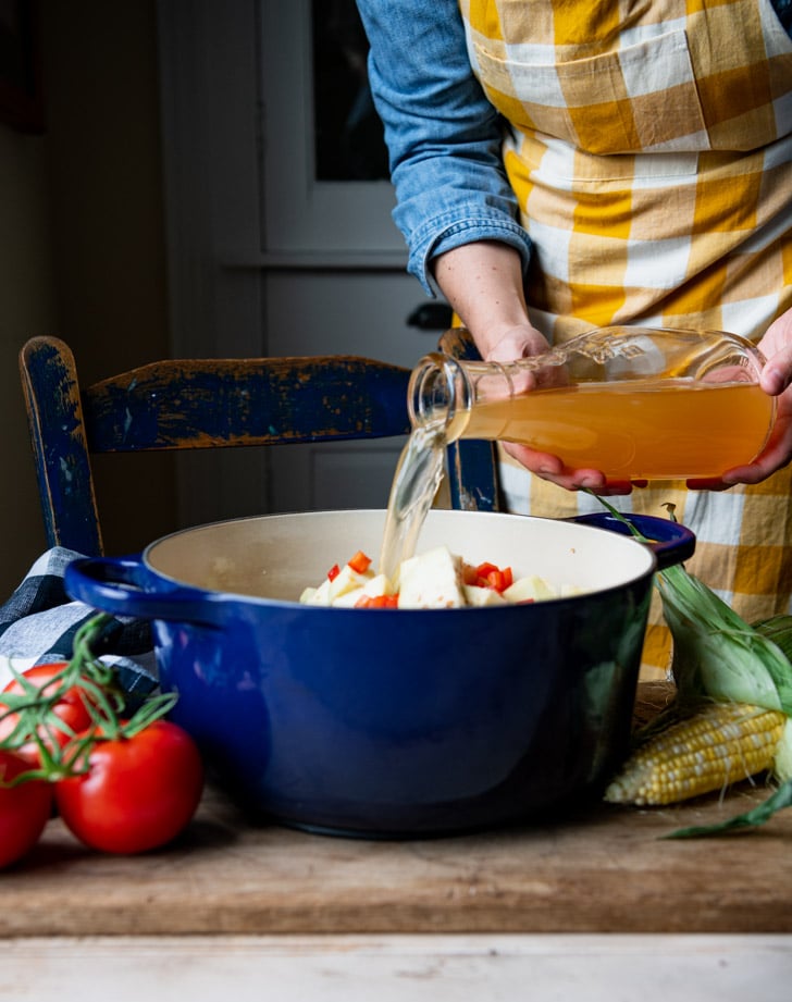 Pouring vegetable broth into a Dutch oven