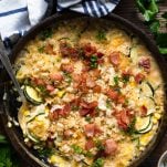 Overhead shot of cheesy zucchini gratin with corn and bacon in a cast iron skillet on a wooden table