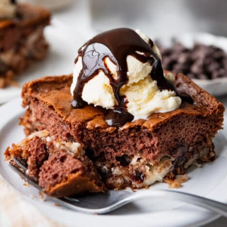 Square side shot of a slice of earthquake cake with a scoop of vanilla ice cream and a drizzle of chocolate syrup.