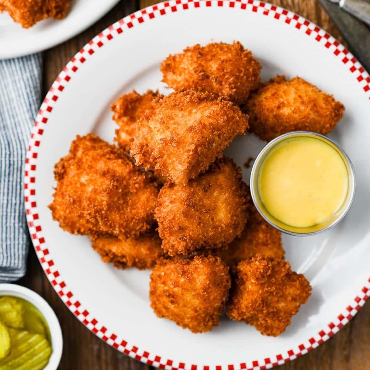Square overhead shot of a plate of homemade chicken nuggets with honey mustard sauce for dipping.