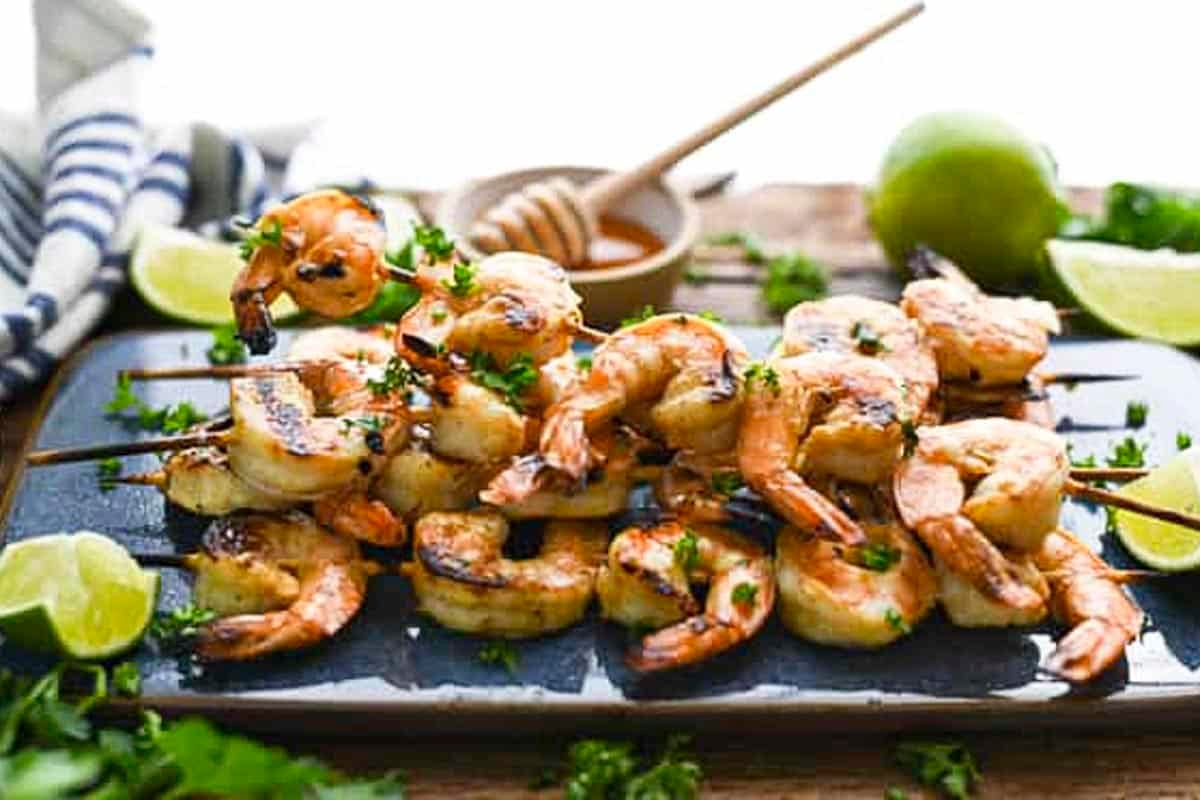 Horizontal side shot of grilled marinated shrimp skewers on a blue serving tray.