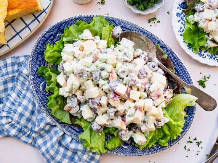 Horizontal overhead shot of a Waldorf salad served on a bed of lettuce on a blue and white platter.