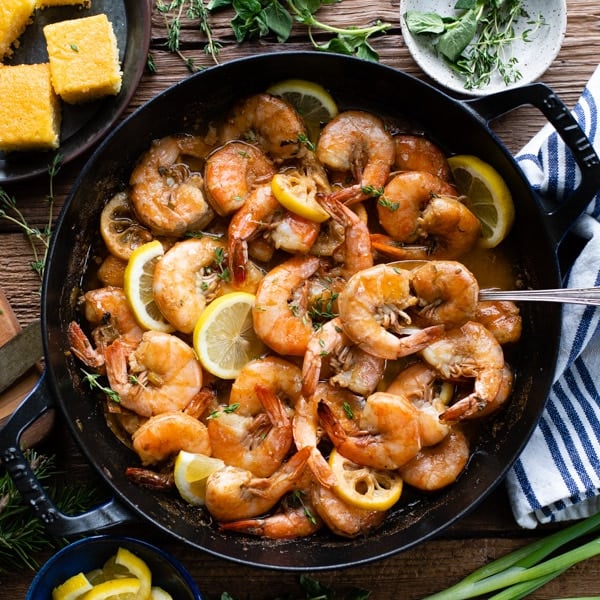 A square overhead image of freshly baked New Orleans style BBQ shrimp in a cast iron skillet.