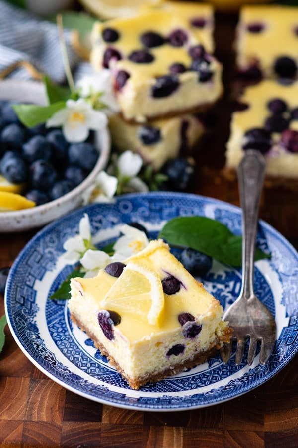 Plate with a lemon cheesecake bar with fresh blueberries on a wooden board