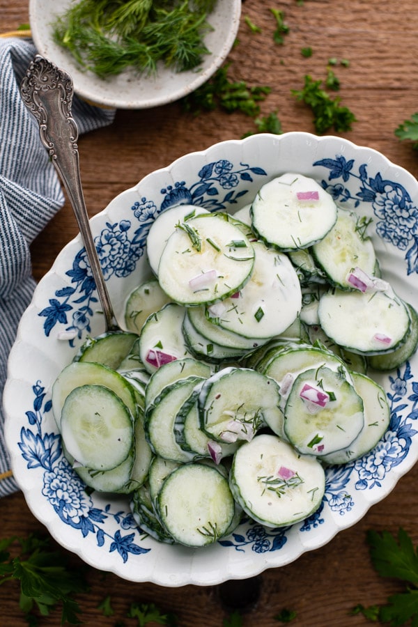 Overhead image of a bowl of creamy cucumber salad with a silver serving spoon