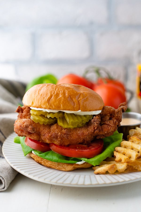Plate of a homemade fried chicken sandwich recipe in front of a white brick backdrop