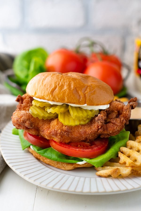 Side shot of a homemade fried chicken sandwich on a plate with fries