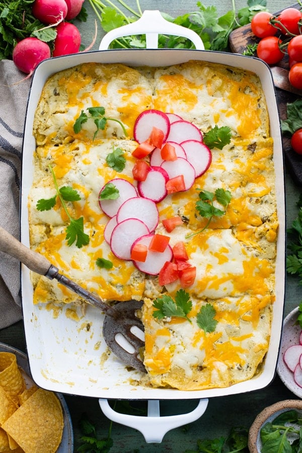 Overhead shot of a wooden spoon in a pan of layered green chile chicken enchilada casserole