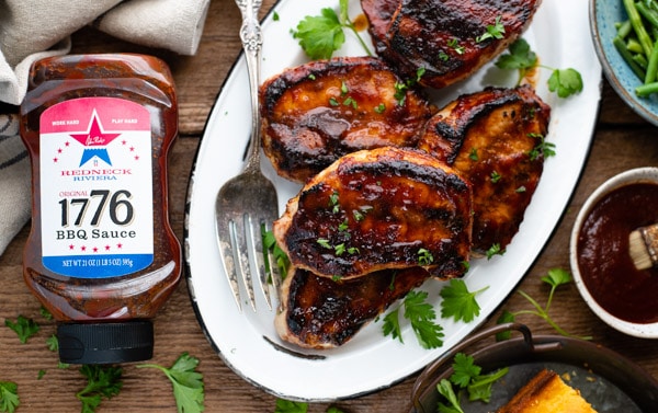 Overhead shot of grilled bbq pork chops on a wooden table with a bottle of barbecue sauce nearby