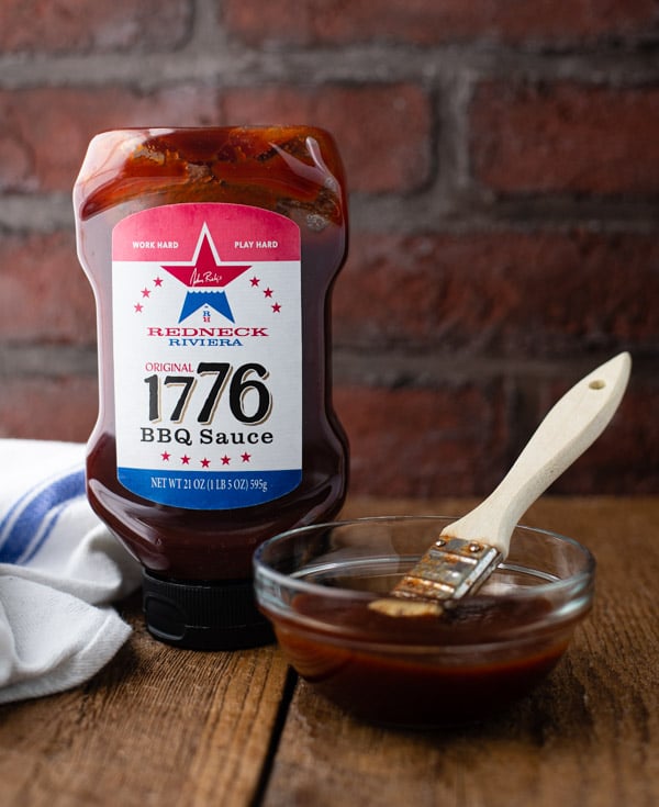 Bottle of 1776 barbecue sauce on a wooden table in front of a brick wall