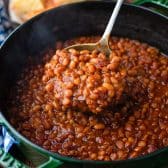 Square image of a ladle serving homemade baked beans with bacon.