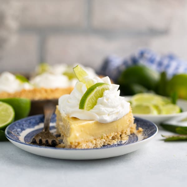 Square side shot of a slice of an authentic key lime pie recipe served on a plate with lots of whipped cream on top