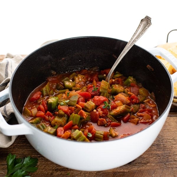 Square side shot of a white Dutch oven with southern okra and tomatoes