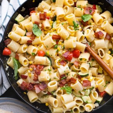 Overhead shot of a cast iron skillet full of pasta with corn zucchini and tomatoes.