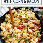 Close up shot of a skillet full of pasta with corn and bacon and text title box at top
