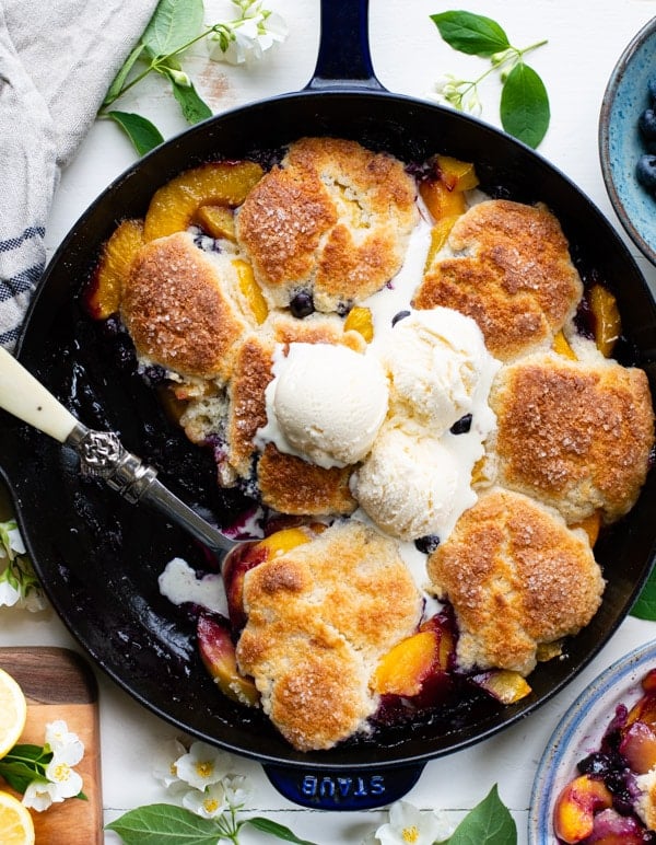 Overhead image of biscuit topped peach cobbler with blueberries in a cast iron skillet