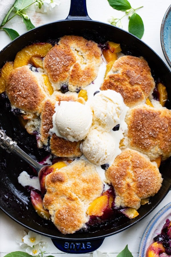 Close overhead shot of old fashioned peach blueberry cobbler in a skillet with vanilla ice cream on top