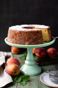 Peach pound cake on a green cake stand with fresh peaches nearby