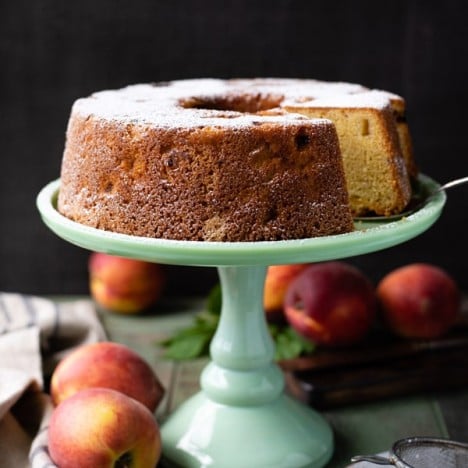 Peach pound cake on a green cake stand with fresh peaches nearby