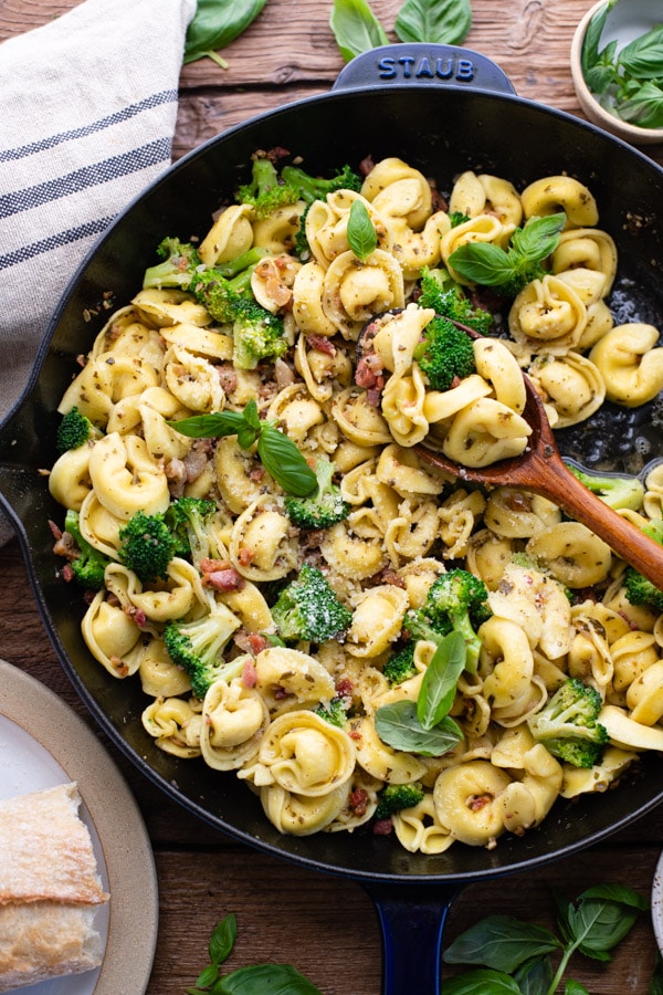 Close up shot of pesto tortellini in a skillet with a wooden spoon