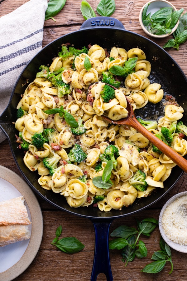 Overhead shot of a skillet of cheese tortellini recipe with pesto on a wooden table
