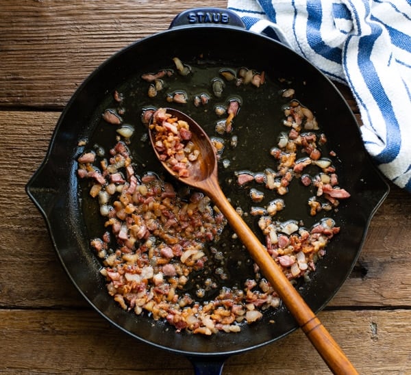 Pancetta in a cast iron skillet with wooden spoon