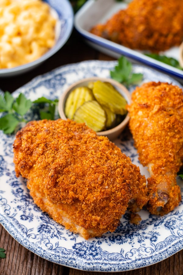 A close up image of two pieces of golden-brown oven-fried Ranch chicken served on a plate with bread and butter pickles.