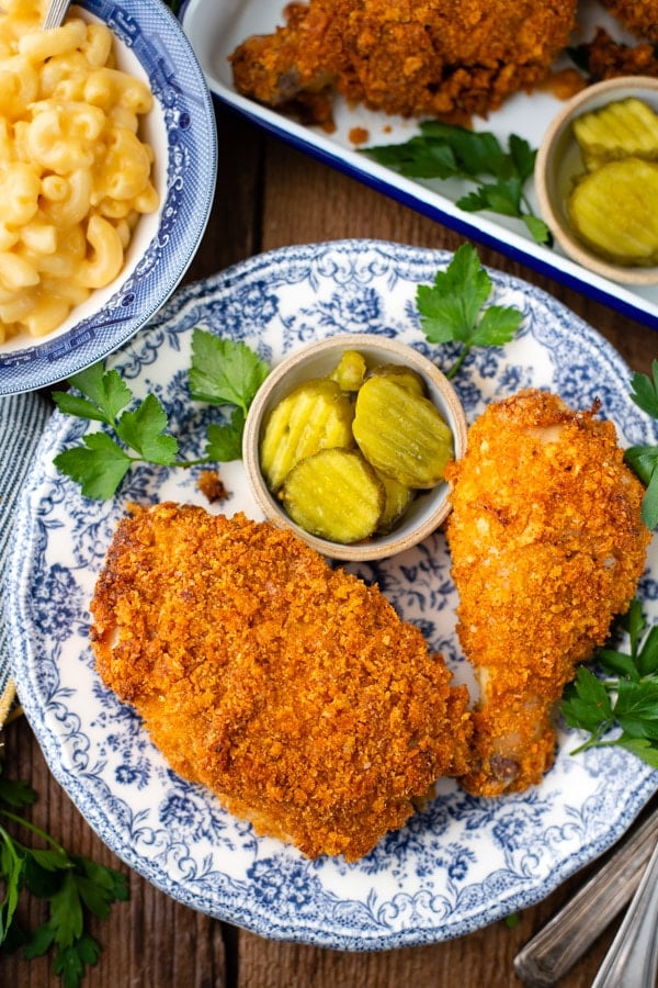 An overhead image of Ranch chicken thigh and drumstick served on a plate with a small dish of bread and butter pickle slices and mac and cheese.